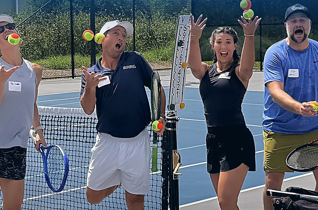 Adult campers juggling tennis balls at the net during a RacFit Adult Tennis Camp weekend in Buda, Texas