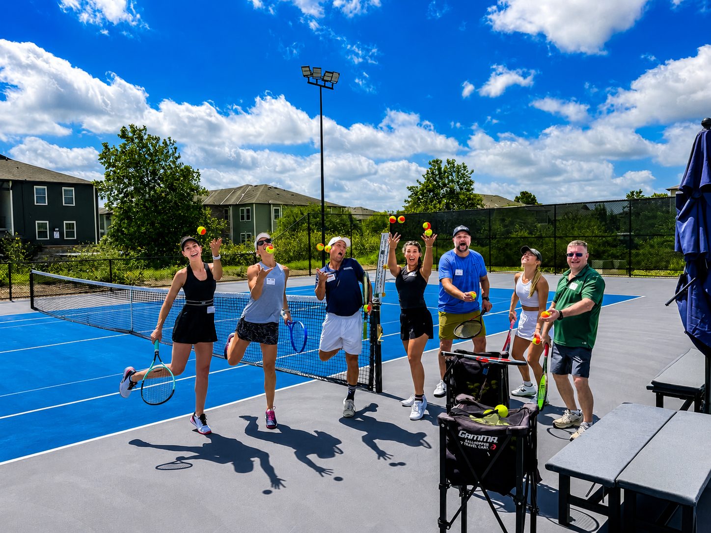 Adult tennis clinic players juggling balls on an outdoor court at RacFit in Buda, Texas