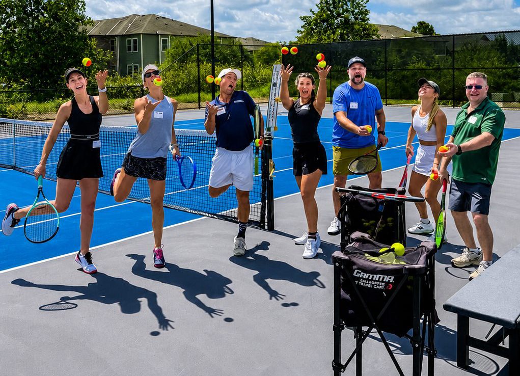 Adult tennis clinic players juggling balls on an outdoor court at RacFit in Buda, Texas
