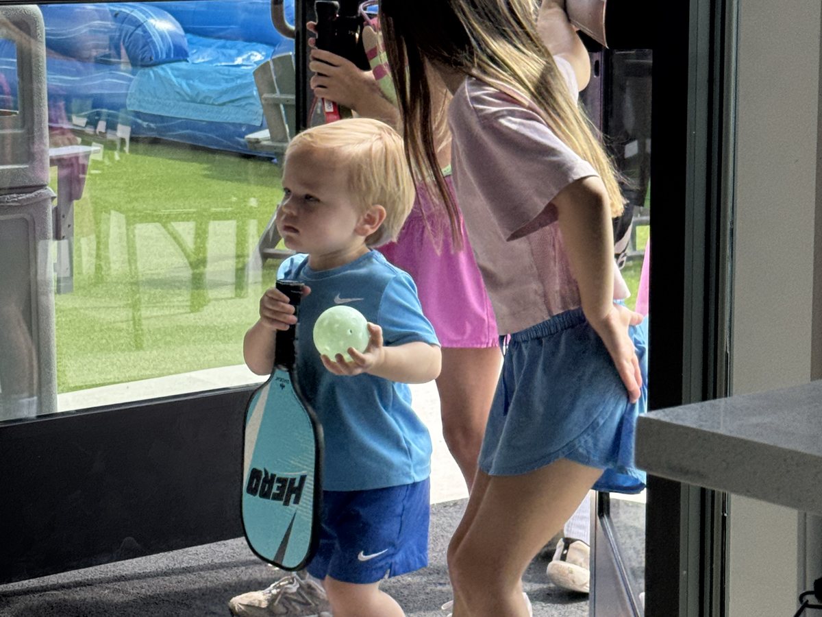Toddler holding a pickleball paddle and ball at RacFit in Buda, Texas