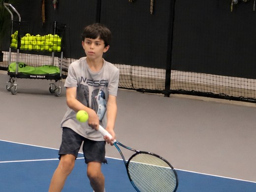 Junior player setting up a backhand on the indoor court during a Green Ball tennis class at RacFit in Buda, Texas