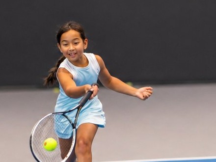 Junior player running down a forehand on the indoor court during an Orange Ball tennis class at RacFit in Buda, Texas