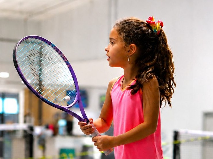 Junior player in ready position holding her racquet on the indoor court during a Red Ball tennis class at RacFit in Buda, Texas