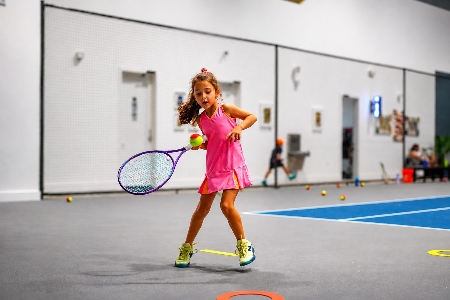 Young girl hitting a forehand with a red ball during a junior tennis lesson on the indoor courts at RacFit in Buda, Texas
