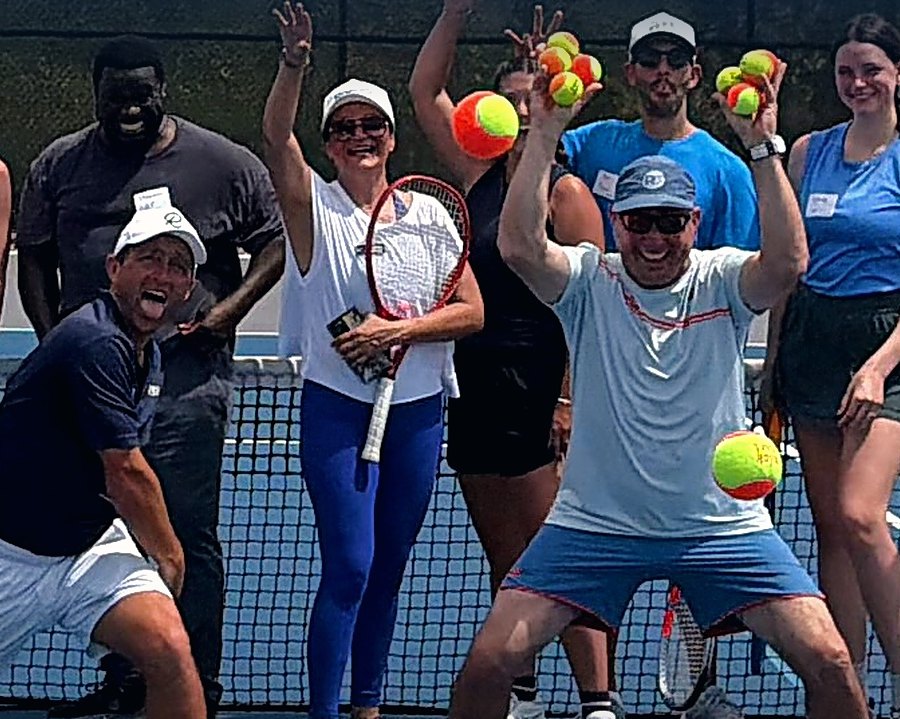 Adult beginners celebrating on court at the end of a Kick Starter tennis clinic at RacFit in Buda, Texas