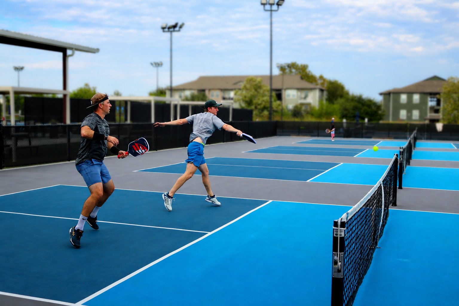 Two members playing doubles pickleball on the outdoor courts at RacFit in Buda, Texas
