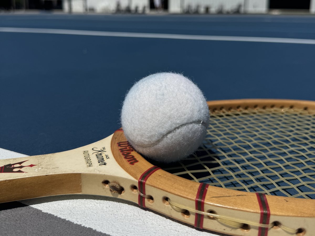 A vintage Wilson wood racquet and ball resting on the baseline at RacFit in Buda, Texas