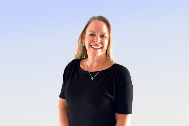 Smiling woman in black shirt with pendant.