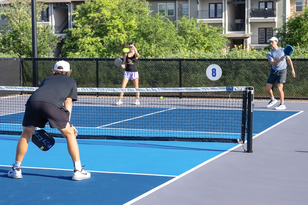 Three people playing pickleball on outdoor court